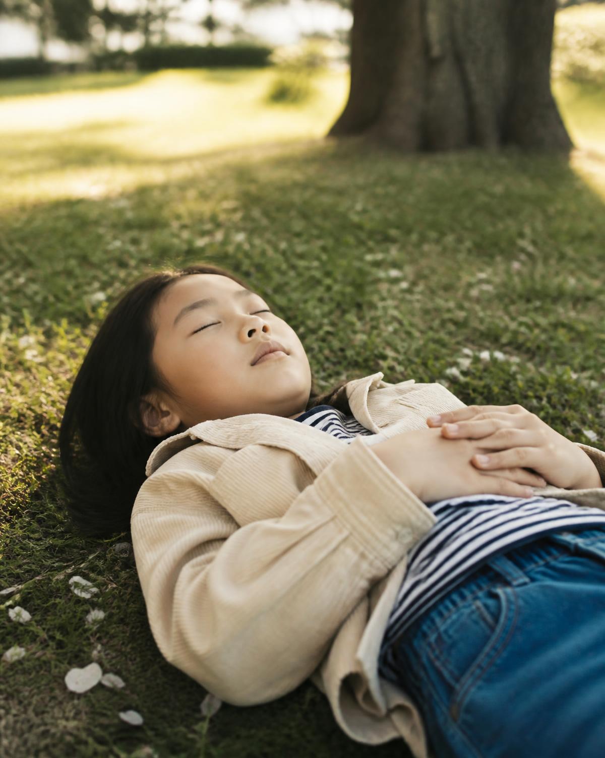 Niña recostada sobre el pasto respirando con calma bajo un árbol