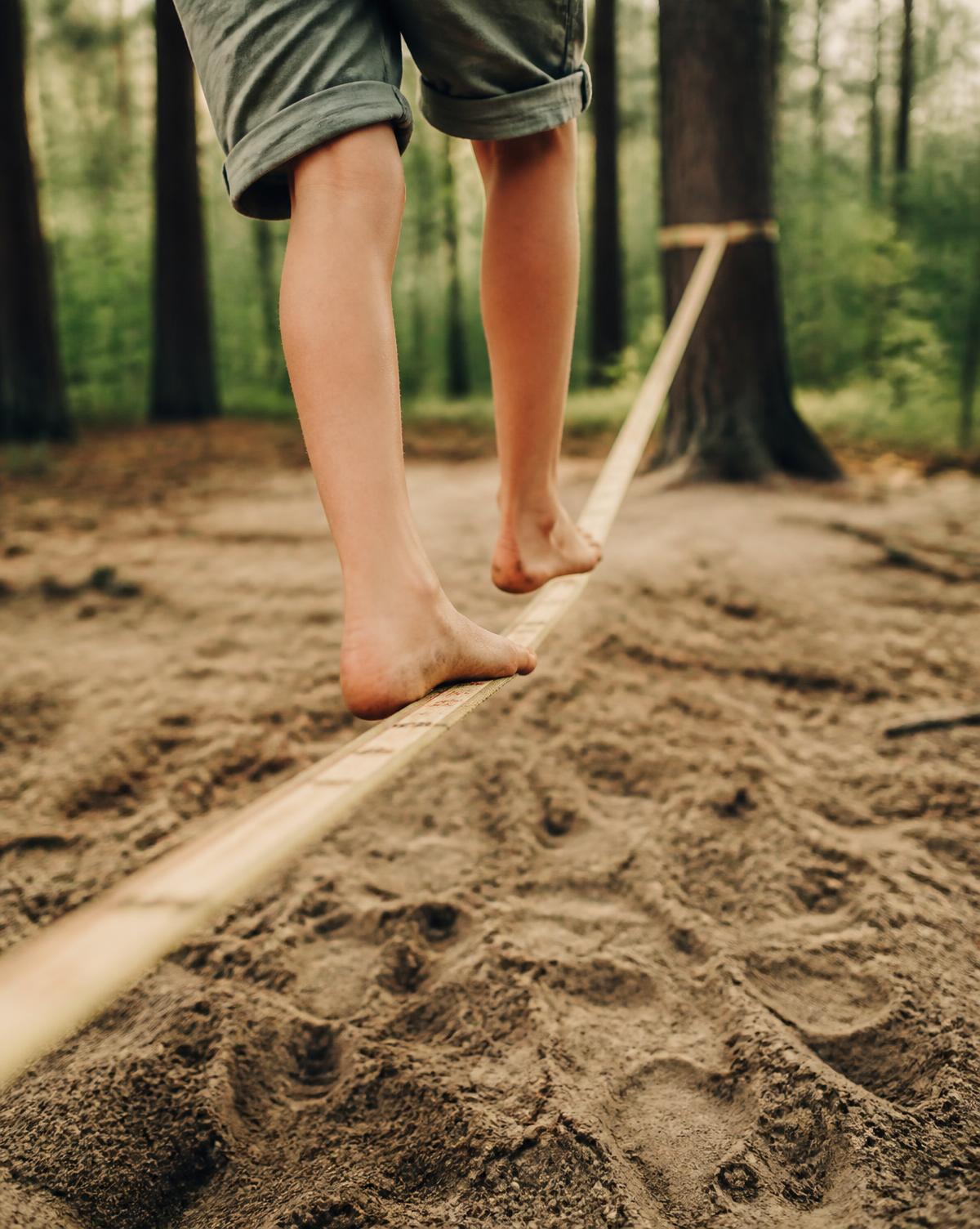 Pies descalzos de una niña caminando sobre una slackline entre los árboles
